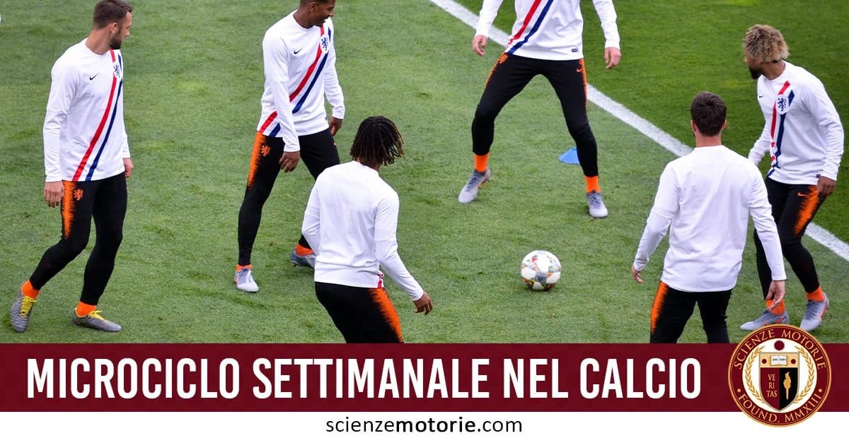 Gruppo di calciatori in riscaldamento su un campo, disposti in cerchio intorno a un pallone da calcio. Indossano maglie bianche con striscia blu e rossa, pantaloni neri con dettagli arancioni e scarpe sportive grigie/arancioni. l'immagine è accompagnata dalla scritta "Microciclo settimanale nel calcio" e dal logo di ScienzeMotorie.com