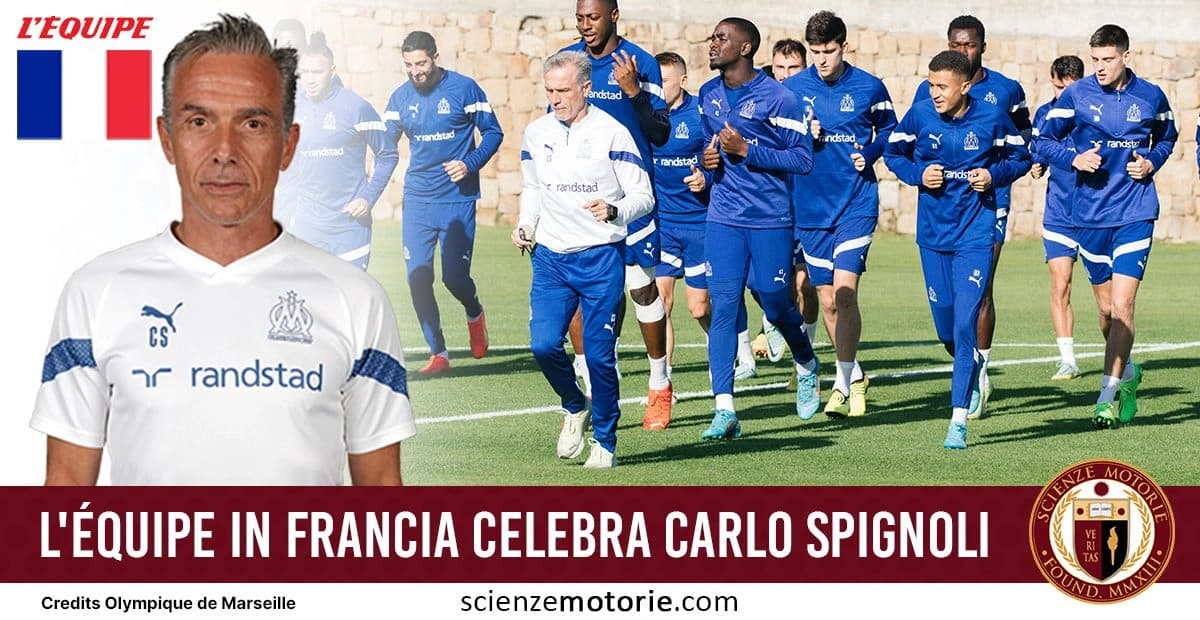 Gruppo di calciatori dell'Olympique de Marseille che corrono in campo con tute blu, accompagnati dall'immagine di Carlo Spignoli in primo piano con la maglia bianca del club. Logo di "L'ÉQUIPE" e bandiera francese in alto a sinistra. Testo in basso: "L'ÉQUIPE in Francia celebra Carlo Spignoli" è accompagnata dal logo di Scienze Morotie.com