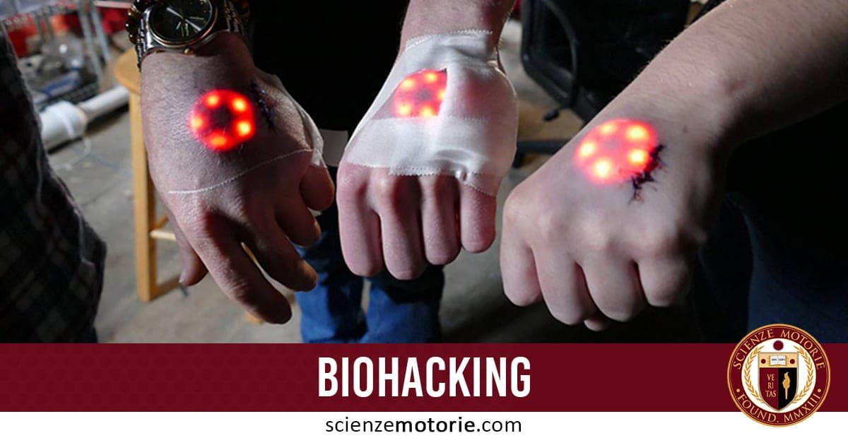 Tre mani con impianti tecnologici visibili sotto la pelle che emettono luci rosse; due mani con bende e una con punti di sutura, con testo “BIOHACKING” e logo Scienze Motorie.