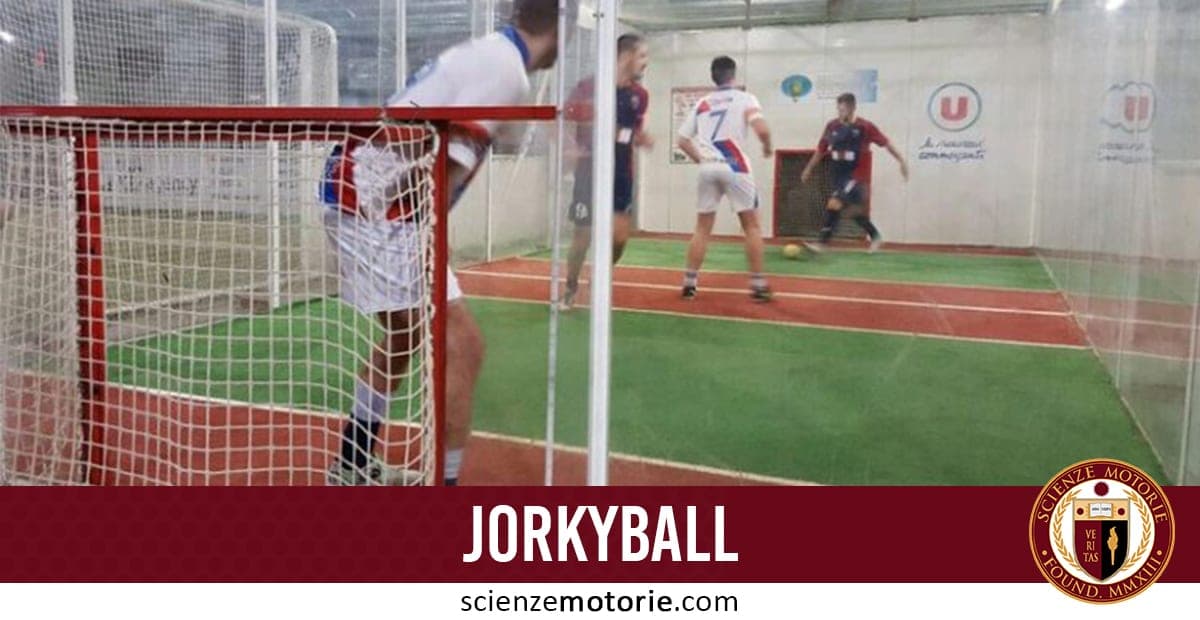 Giocatori che disputano una partita di jorkyball su un campo indoor delimitato da pareti trasparenti.