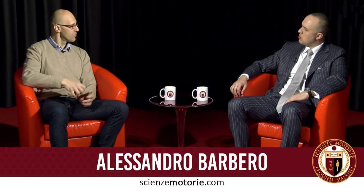 Due uomini seduti su poltrone rosse durante un'intervista. Uno indossa un maglione beige, l'altro un abito elegante a righe. Tra loro un tavolino con due tazze. Sullo sfondo, una tenda nera. In basso si legge "Alessandro Barbero" e il logo di Scienze Motorie con l'indirizzo web.