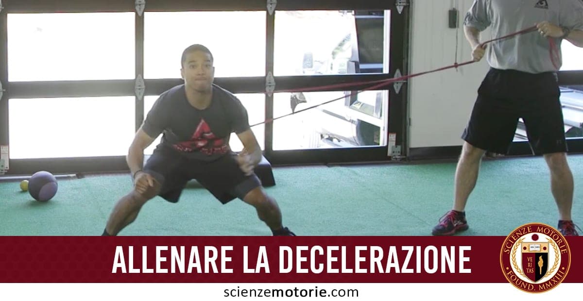 Due persone in palestra eseguono un esercizio con fascia elastica; una è in semi-accosciata con la fascia legata alla vita, l’altra controlla la tensione.