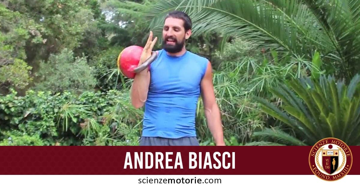 Uomo con barba e capelli scuri che solleva un kettlebell rosso all'aperto, circondato da alberi. Indossa una maglietta blu senza maniche. In basso si leggono un nome e il sito scienzemotorie.com.