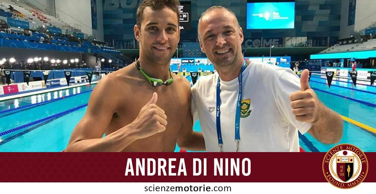 Due uomini sorridenti in posa accanto a una piscina di competizione, entrambi fanno il gesto del pollice in su. Sullo sfondo si vedono le gradinate.