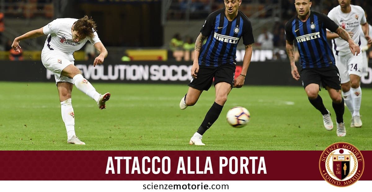 Partita di calcio con un giocatore in maglia bianca che calcia il pallone verso la porta, mentre due avversari in maglia a righe blu e nere tentano di fermarlo.