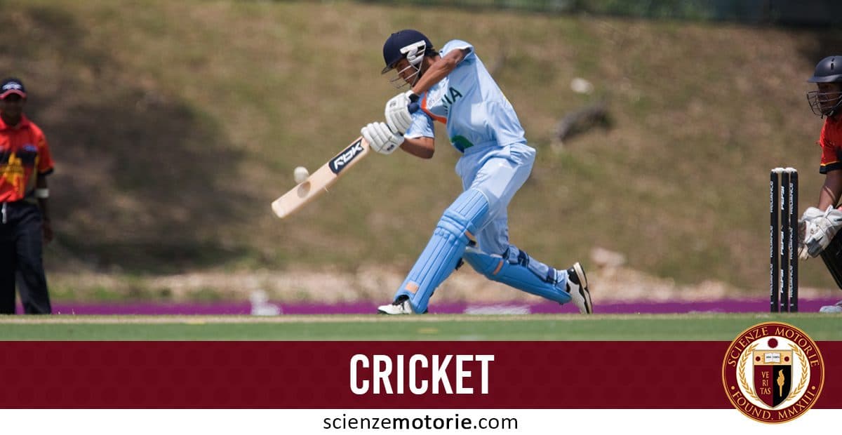 Giocatore di cricket in divisa azzurra che colpisce la palla con la mazza, circondato da avversari in campo.