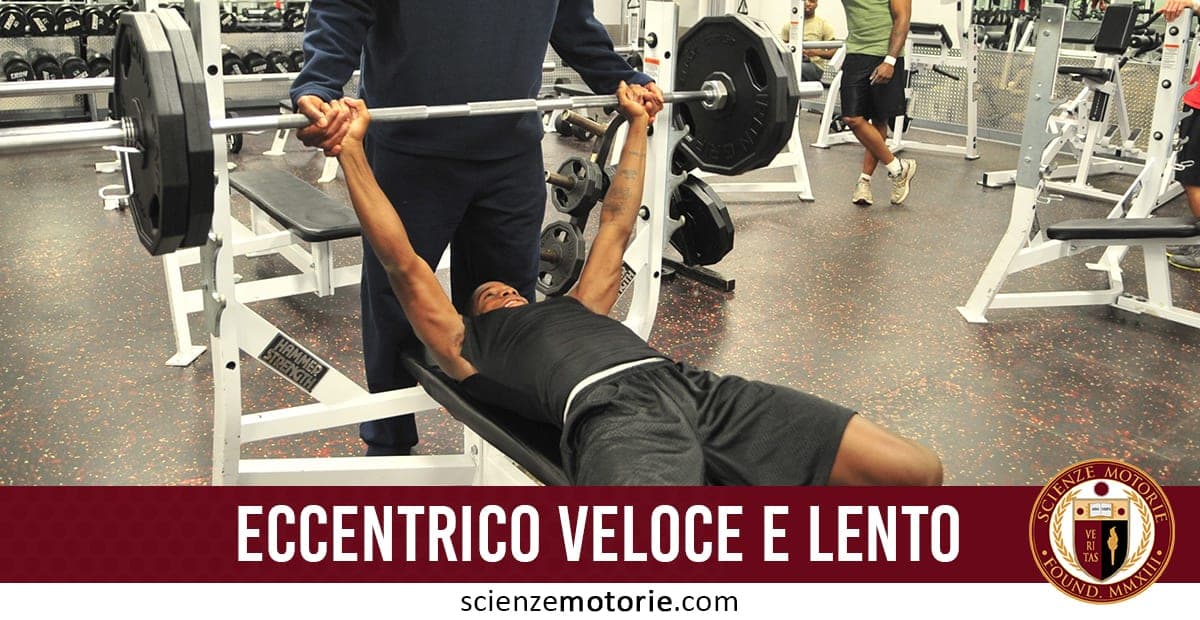 Nell'immagine, ci sono persone in una palestra. Una persona sta facendo sollevamento pesi su panca, assistita da un'altra persona che sembra stia facendo da spotter. Sullo sfondo ci sono altre persone che si allenano. In basso, c'è la scritta "Eccentrico Veloce e Lento" e un logo con "Scienze Motorie".