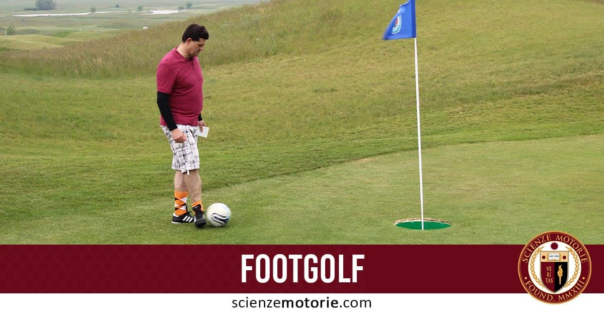 Persona che gioca a footgolf su campo verde, pronta a calciare un pallone da calcio verso una buca con bandierina blu.
