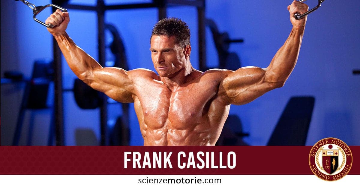 Frank Casillo esegue esercizi con attrezzi in palestra, concentrato sull’allenamento, con attrezzature sullo sfondo e il logo ScienzeMotorie.com.