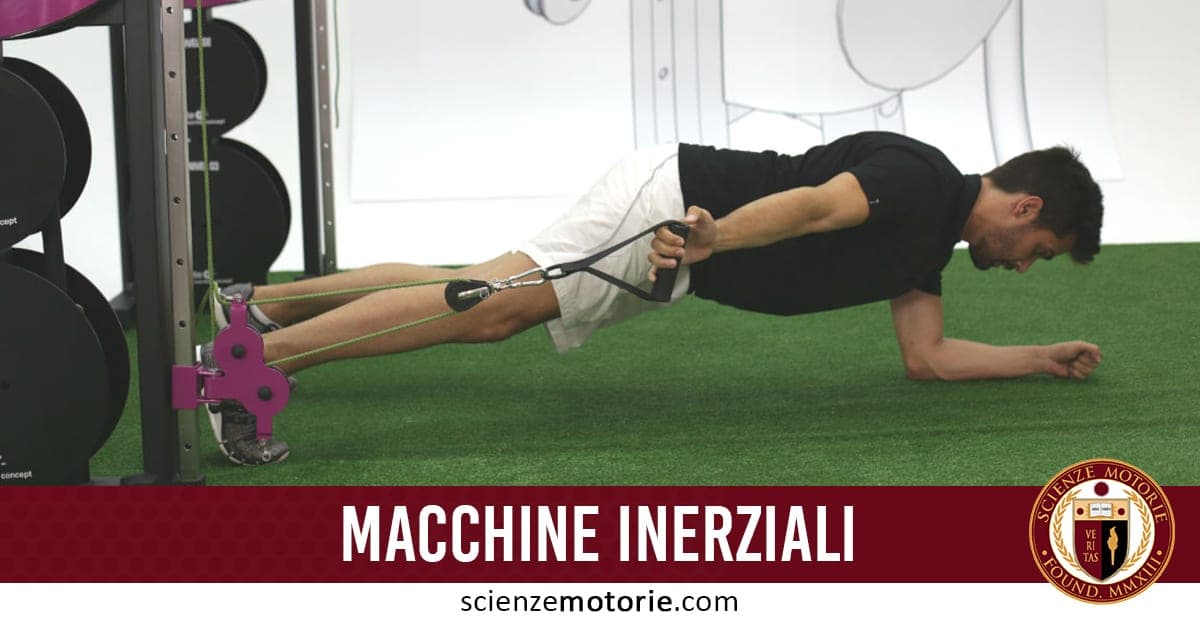 Persona in posizione prona su campo sintetico verde che esegue esercizio con macchina inerziale, afferrando due cavi; sullo sfondo testo “MACCHINE INERZIALI” e logo ScienzeMotorie.com.