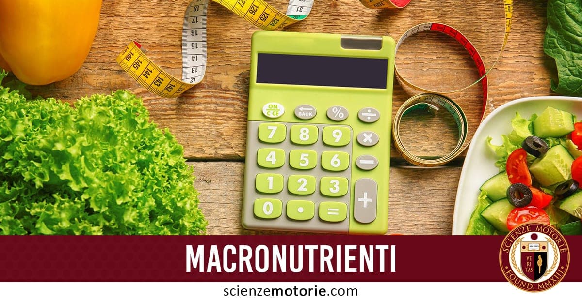 Calcolatrice verde su tavolo di legno con metro da sarta, piatto di insalata con cetrioli, pomodori e olive, verdure fresche e scritta "MACRONUTRIENTI" assieme al logo di ScienzeMotorie.com