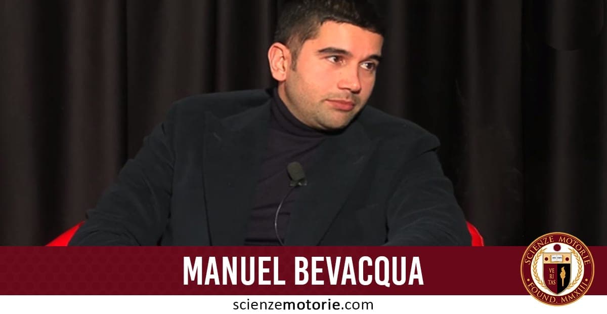 Manuel Bevacqua seduto su una sedia con maglione a collo alto e giacca nera, intervistato davanti a un fondale scuro, con microfono e logo Scienze Motorie.
