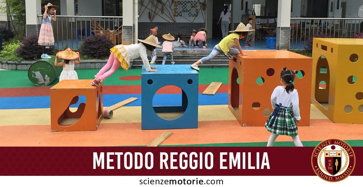 Bambini con cappelli di paglia giocano all’aperto su superficie colorata, arrampicandosi su blocchi arancioni e blu; in basso, scritta “Metodo Reggio Emilia” e logo di ScienzeMotorie.com.
