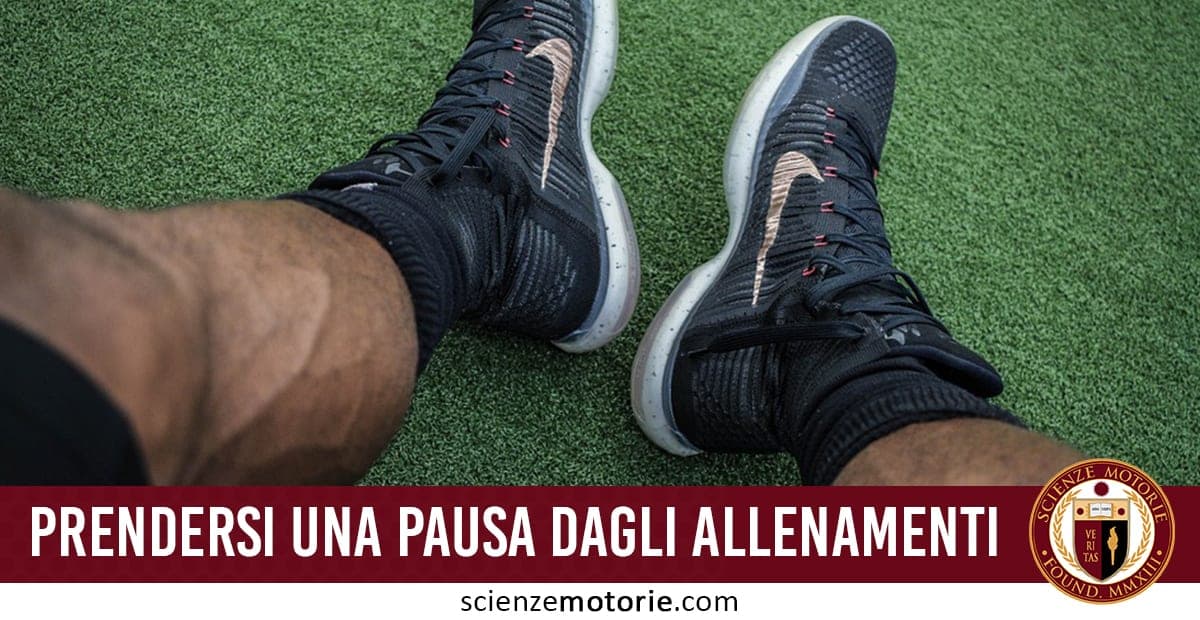 Gambe di persona seduta su prato sintetico con scarpe da ginnastica nere, scritta “Prendersi una pausa dagli allenamenti” e logo di ScienzeMotorie.com.