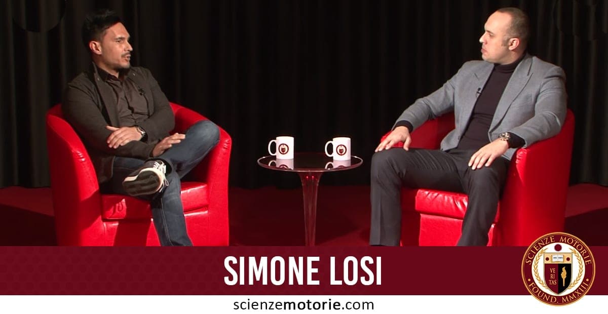 Simone Losi e Giacomo Catalani seduti su poltrone rosse durante una conversazione formale con un tavolino e due tazze tra di loro.