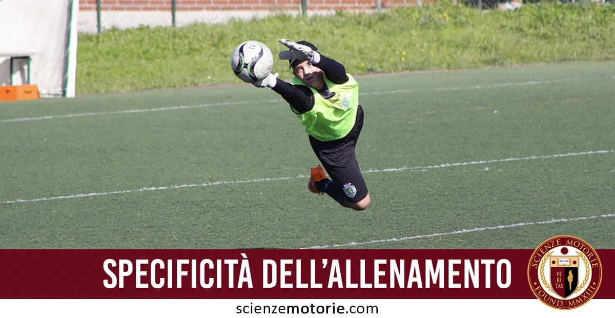 Portiere di calcio in volo mentre para la palla durante un allenamento, con maglia verde e guanti. In basso, scritta "Specificità dell'allenamento" e sito scienzemotorie.com.
