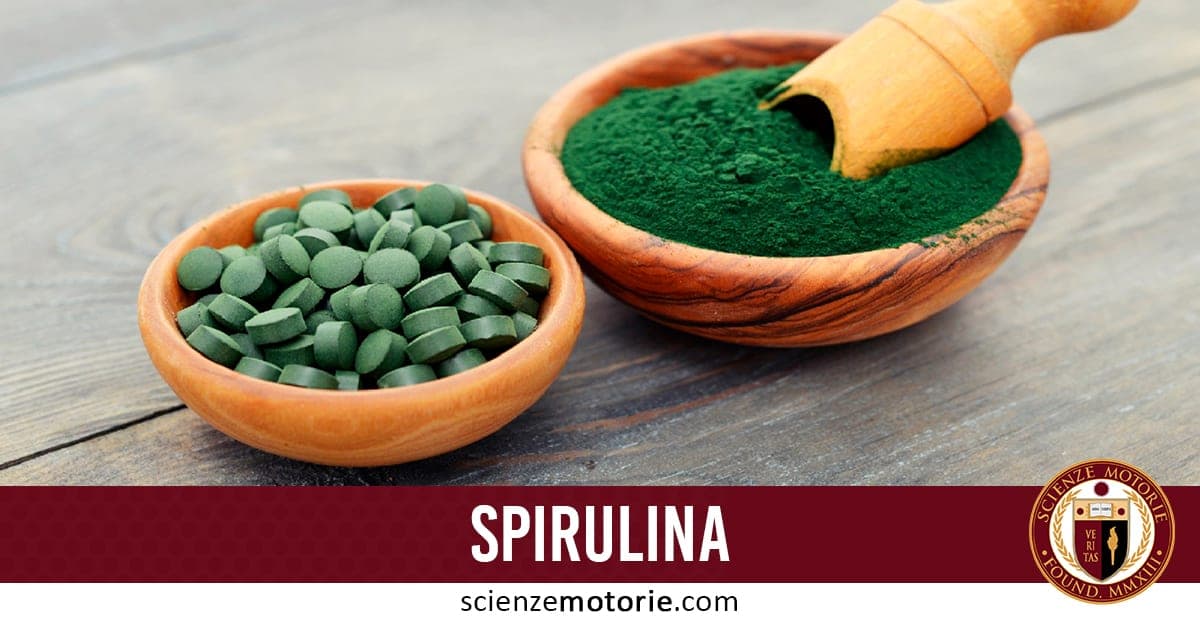 Due ciotole di legno su superficie scura, una con compresse verdi scure di spirulina e l’altra con polvere verde intensa di spirulina con cucchiaio di legno; banda bordeaux con scritta "SPIRULINA" e logo scienzemotorie.com