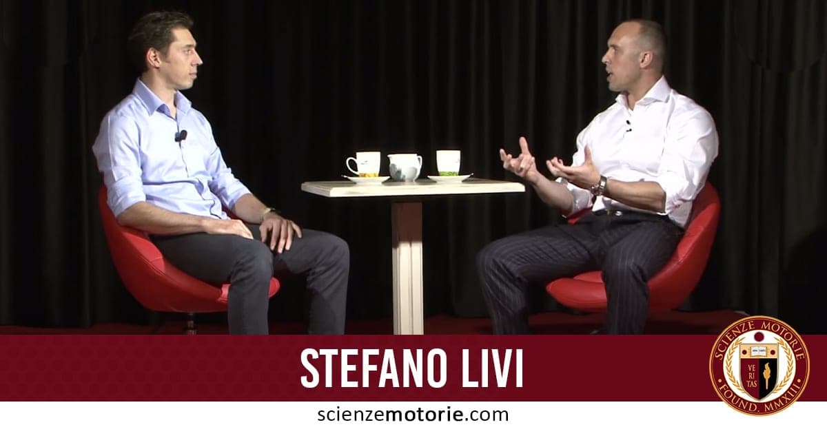 Stefano Livi e Giacomo Catalani seduti su sedie rosse con microfoni, davanti a un tavolino bianco con tazze. Sfondo con tenda nera e logo Scienze Motorie in basso.