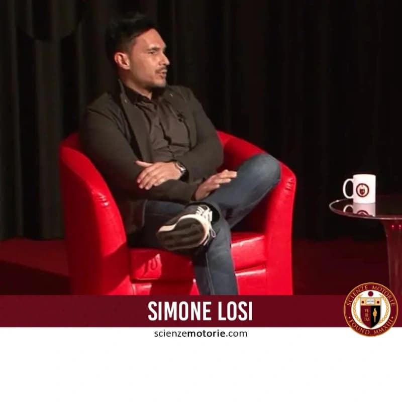 Simone Losi e Giacomo Catalani seduti su poltrone rosse durante una conversazione formale con un tavolino e due tazze tra di loro.