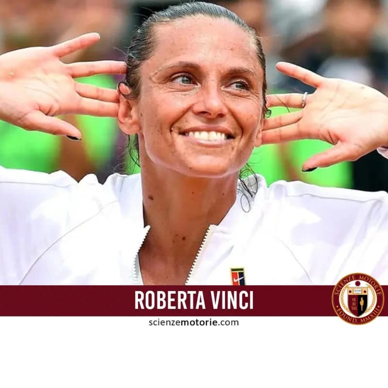 Roberta Vinci in primo piano con giacca sportiva bianca, sorridente con mani alzate in gesto di celebrazione. Logo ITF visibile sulla spalla destra della giacca. Sfondo sfocato di un campo da tennis.