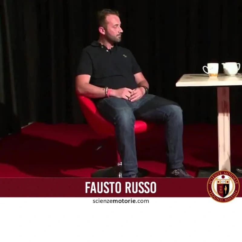 Uomo seduto su poltrona rossa con tavolino e tazze bianche, fascia bordeaux con nome Fausto Russo e logo Scienze Motorie.