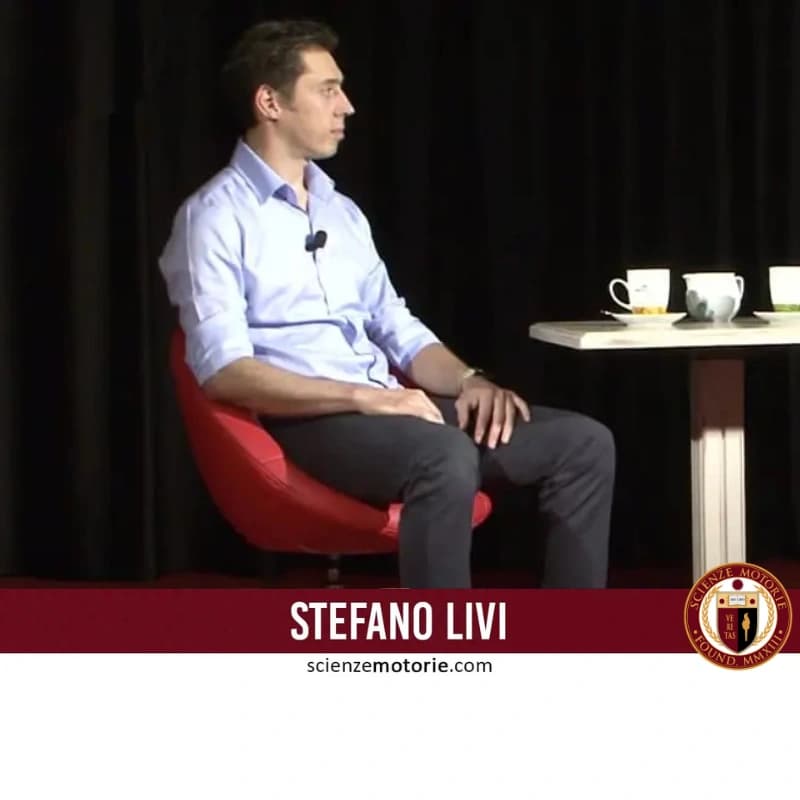 Stefano Livi seduto su poltrona rossa con tavolino e tazze bianche, fascia bordeaux con nome e logo Scienze Motorie.